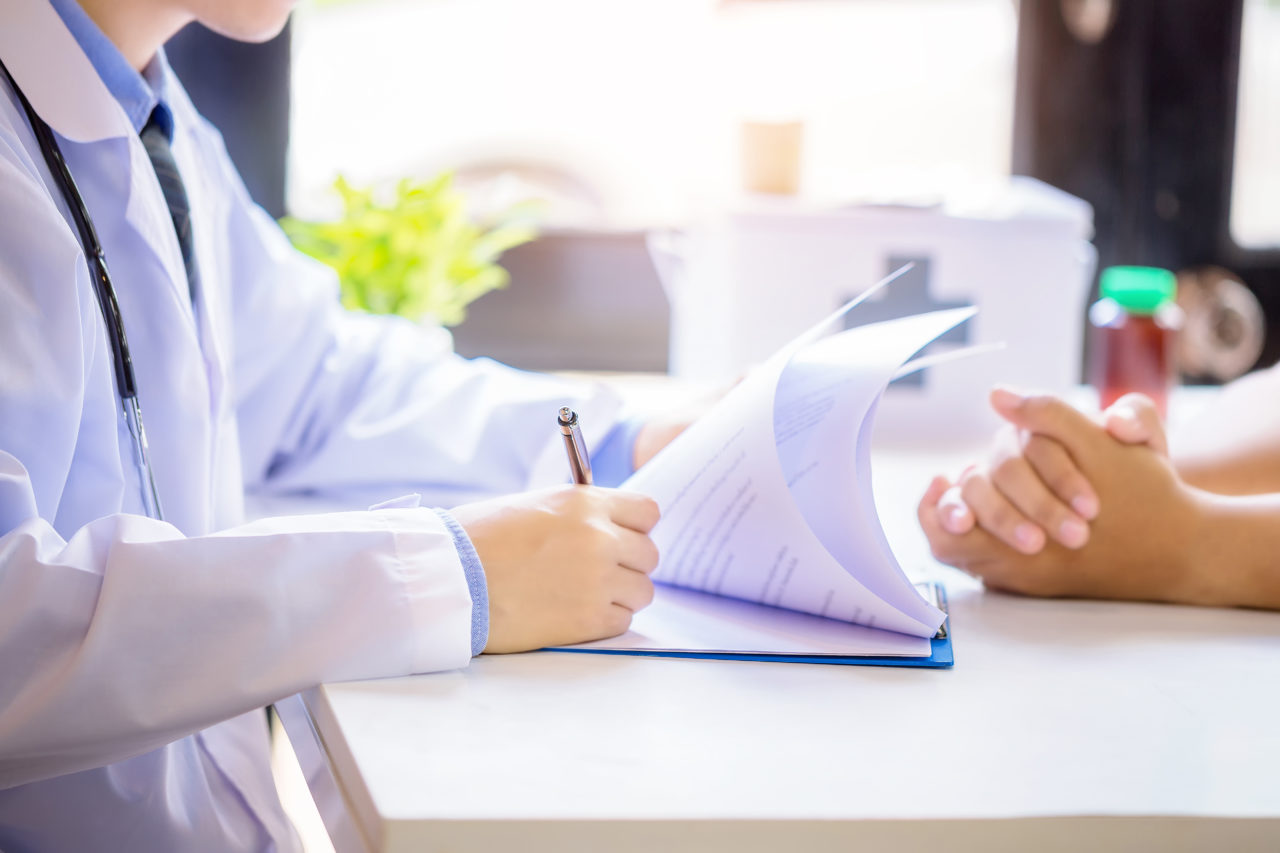 Male doctor consulting patient while filling up an application form at the desk in hospital.